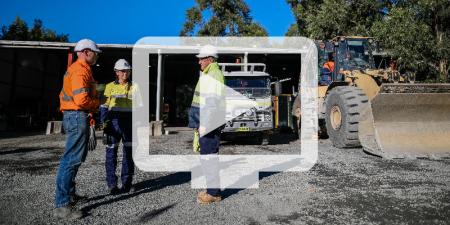 Image of three people wearing Hi-vis standing near a shed and machinery. The image has a translucent video icon overlaid.