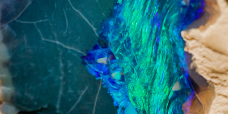 Close up photograph of an opal surrounded by dirt found at Lightning Ridge.
