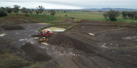 A quarried landscape with machinery at the base of a hill. Green fields are in the background.