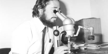 Black and white photo of a scientist looking through a microscope