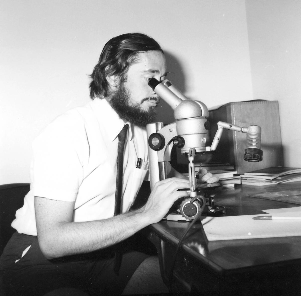 A black and white photo of a scientist looking into a microscope