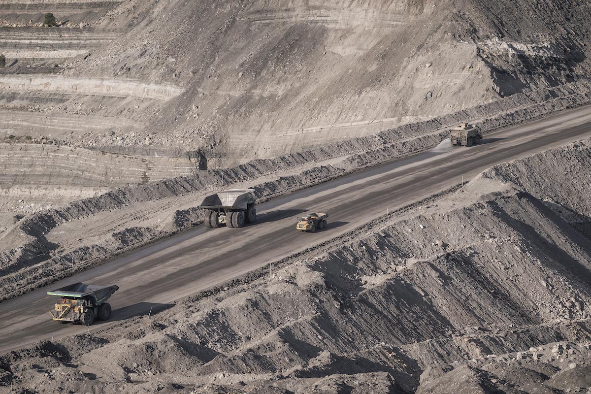 Four trucks on straight road in open cut coal mine.